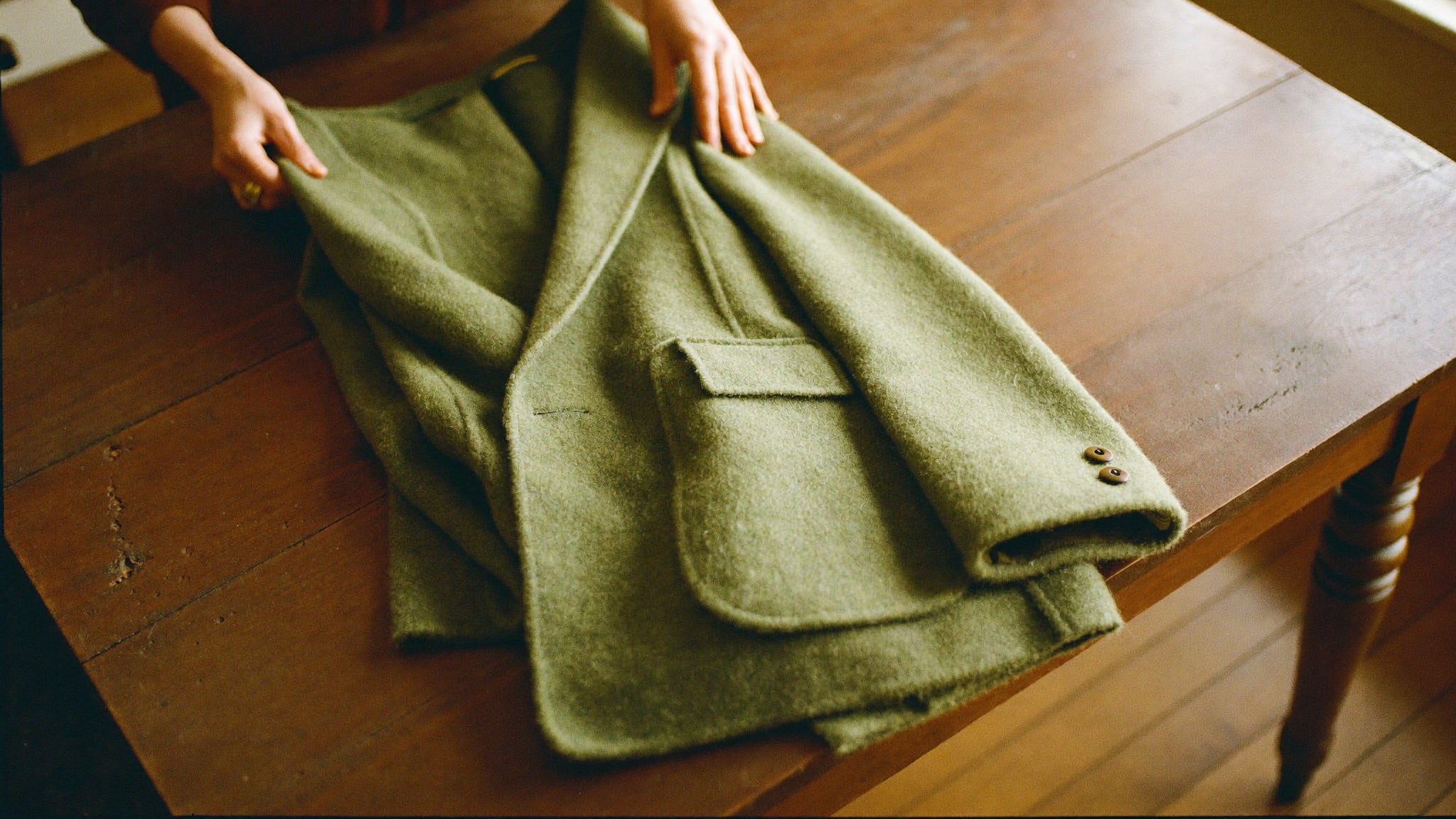 Hands carefully folding a camel wool coat